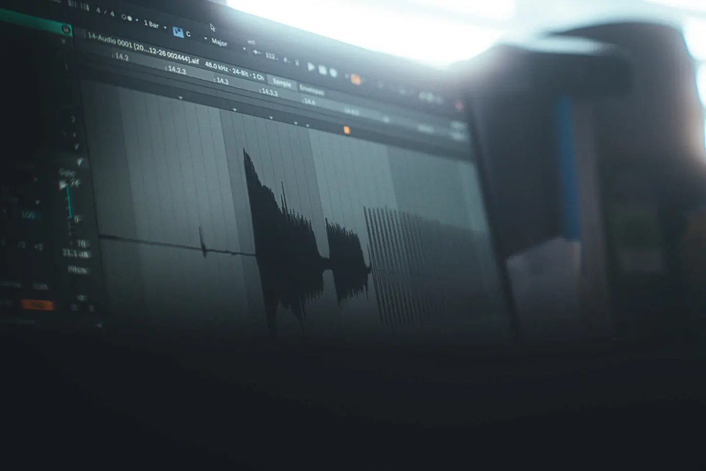 A computer screen showing an audio waveform in a DAW sample editor, shot at an angle in a dim room